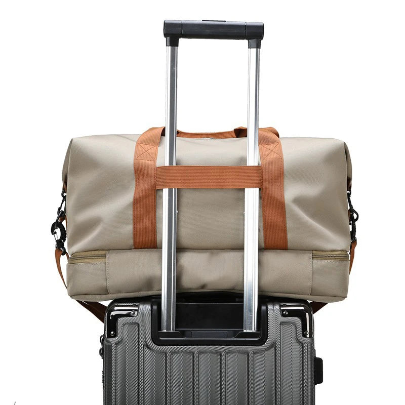 Beige duffel bag with brown accents attached to a gray suitcase on a white background